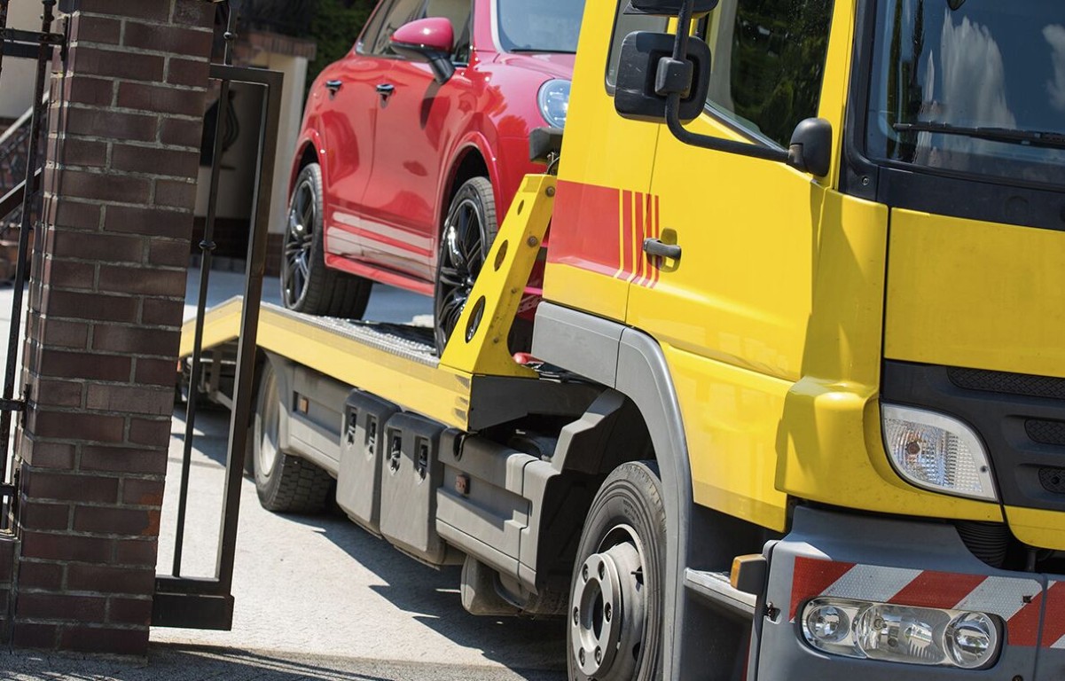 Yellow flatbed tow truck carrying a red car through a residential area in Deer Park, NY
