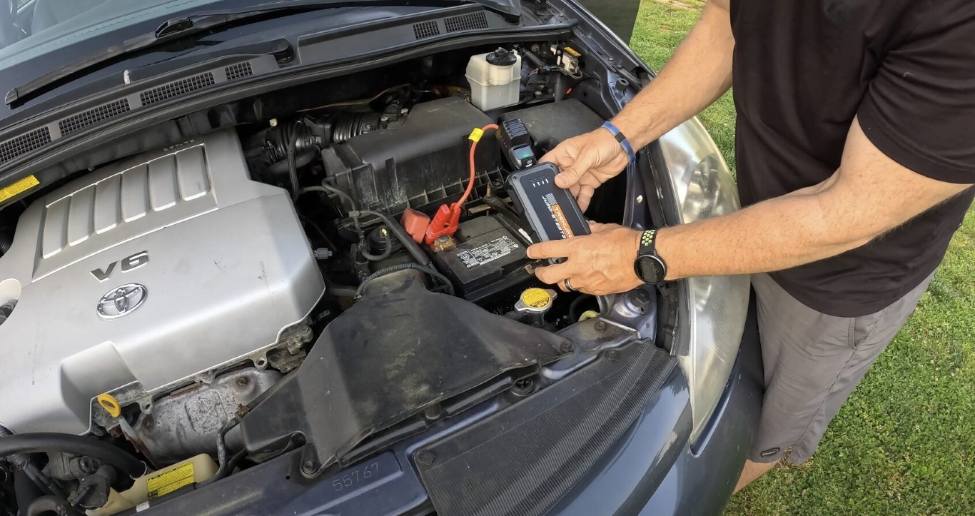 Technician jump starting a dead car battery with cables under the hood