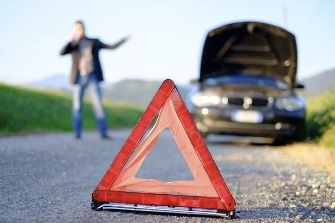 Driver calling for roadside assistance with a broken down car on the side of the road